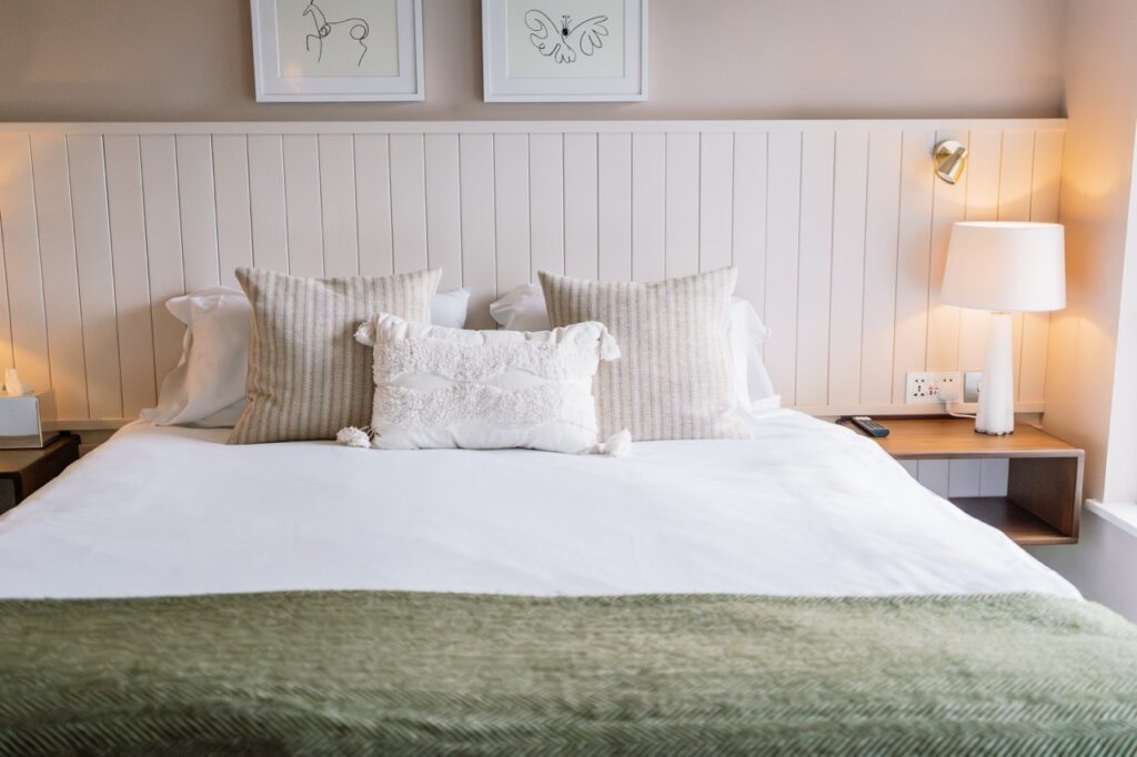 King bed with white linens, two beige striped pillows, and a white textured bolster, flanked by nightstands and a lamp on the right edge of the image.