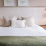 King bed with white linens, two beige striped pillows, and a white textured bolster, flanked by nightstands and a lamp on the right edge of the image.
