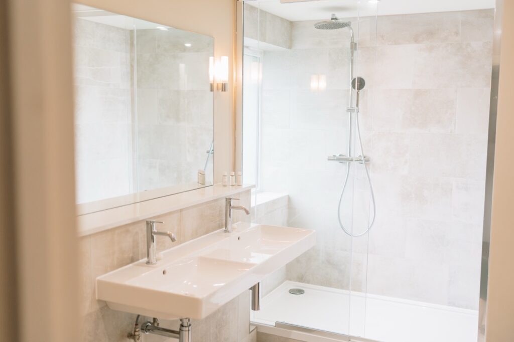 Modern bathroom with a double-sink vanity, large mirror, and glass-enclosed shower with a rainfall head.
