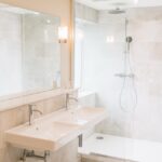 Modern bathroom with a double-sink vanity, large mirror, and glass-enclosed shower with a rainfall head.