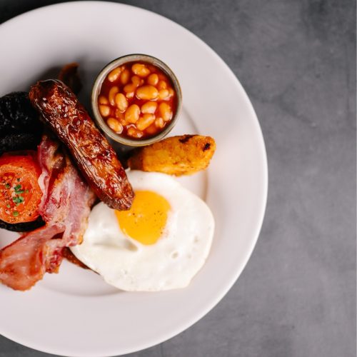 full english breakfast with egg bacon sausage tomato beans and hash browns on a grey background from hatton court hotel